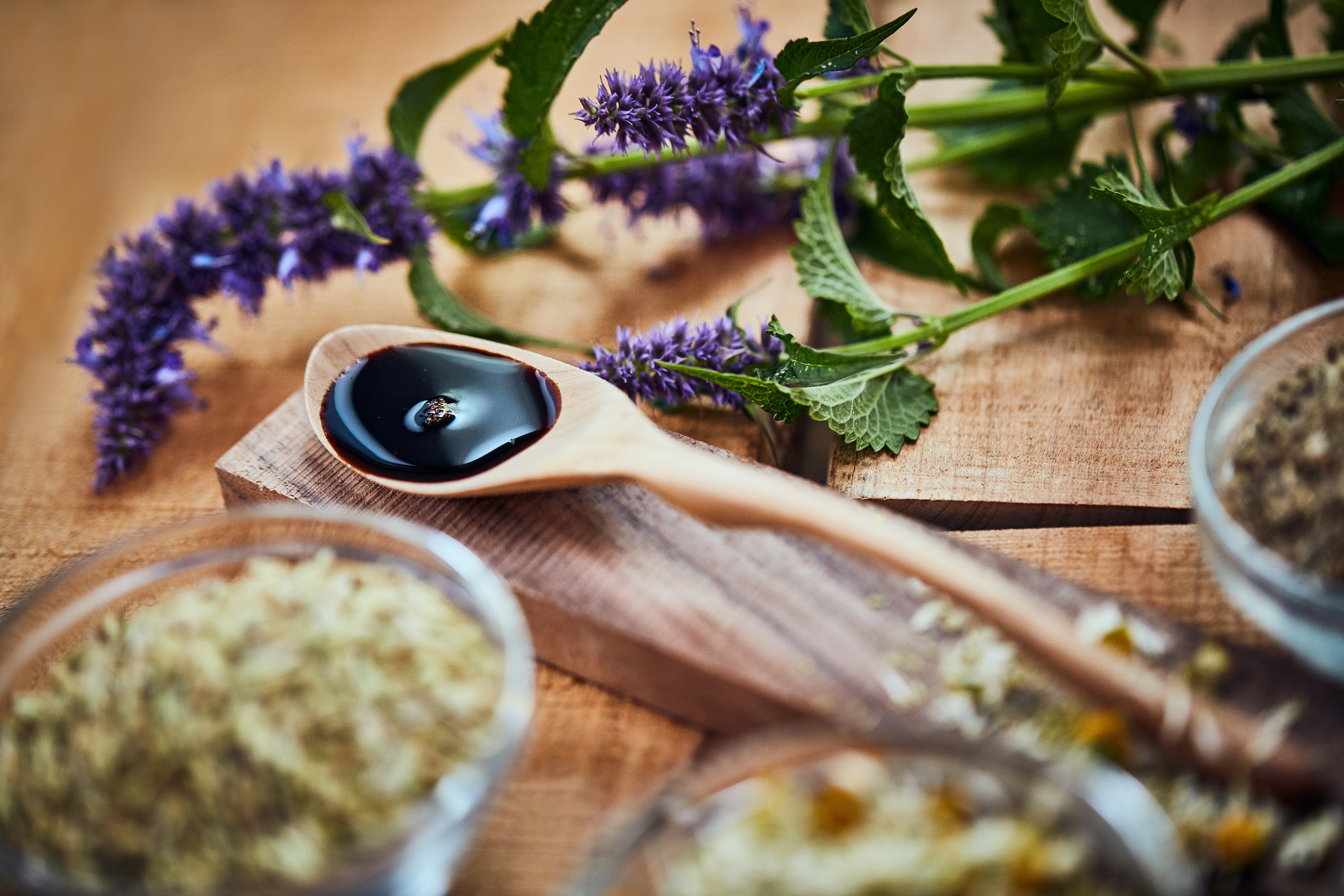 Shot of a wooden spoon with dark liquid in it surrounded by fresh lavender on a table.